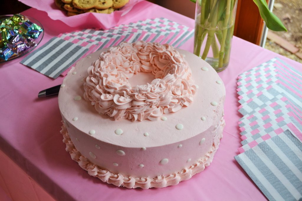 Photo of a pink baby shower cake on a table with a pink table cloth.