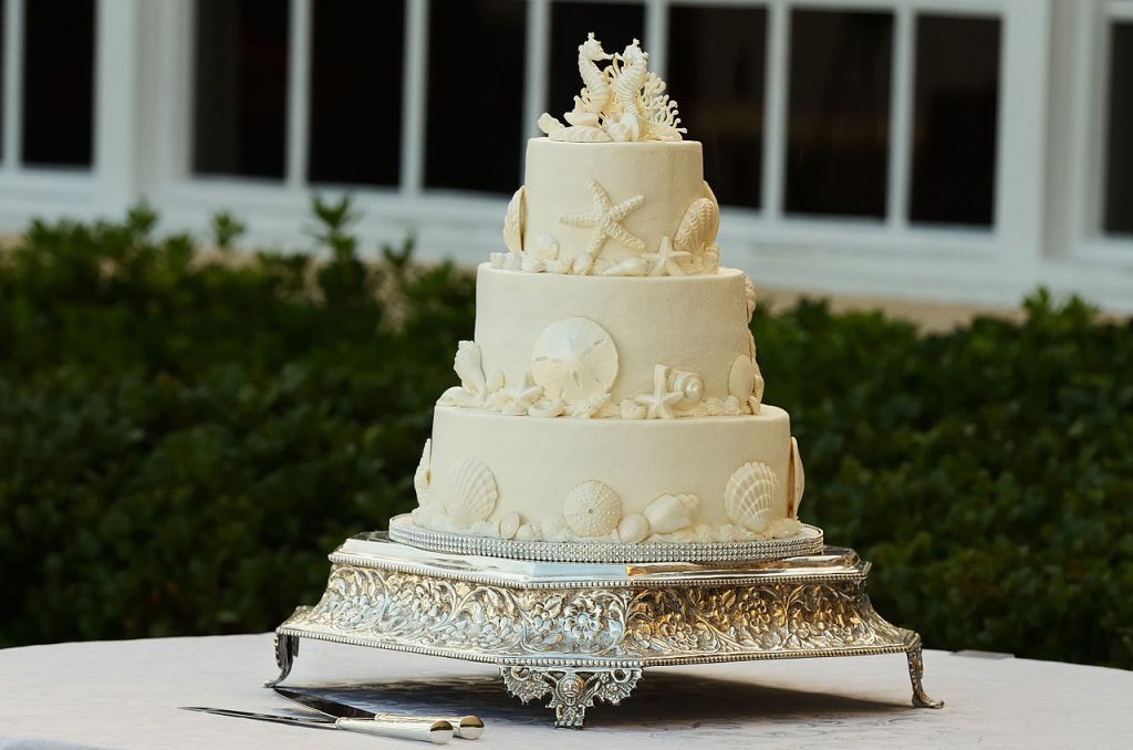 a super fancy white wedding cake sits on a platter on a table