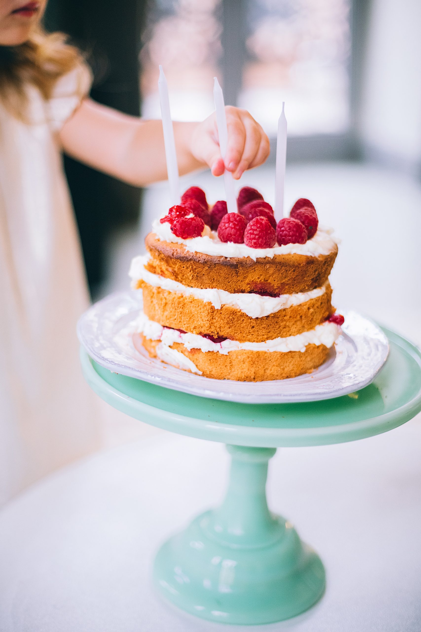 child putting candle sticks on a 3 layer simple cake topped with icing and strawberries 